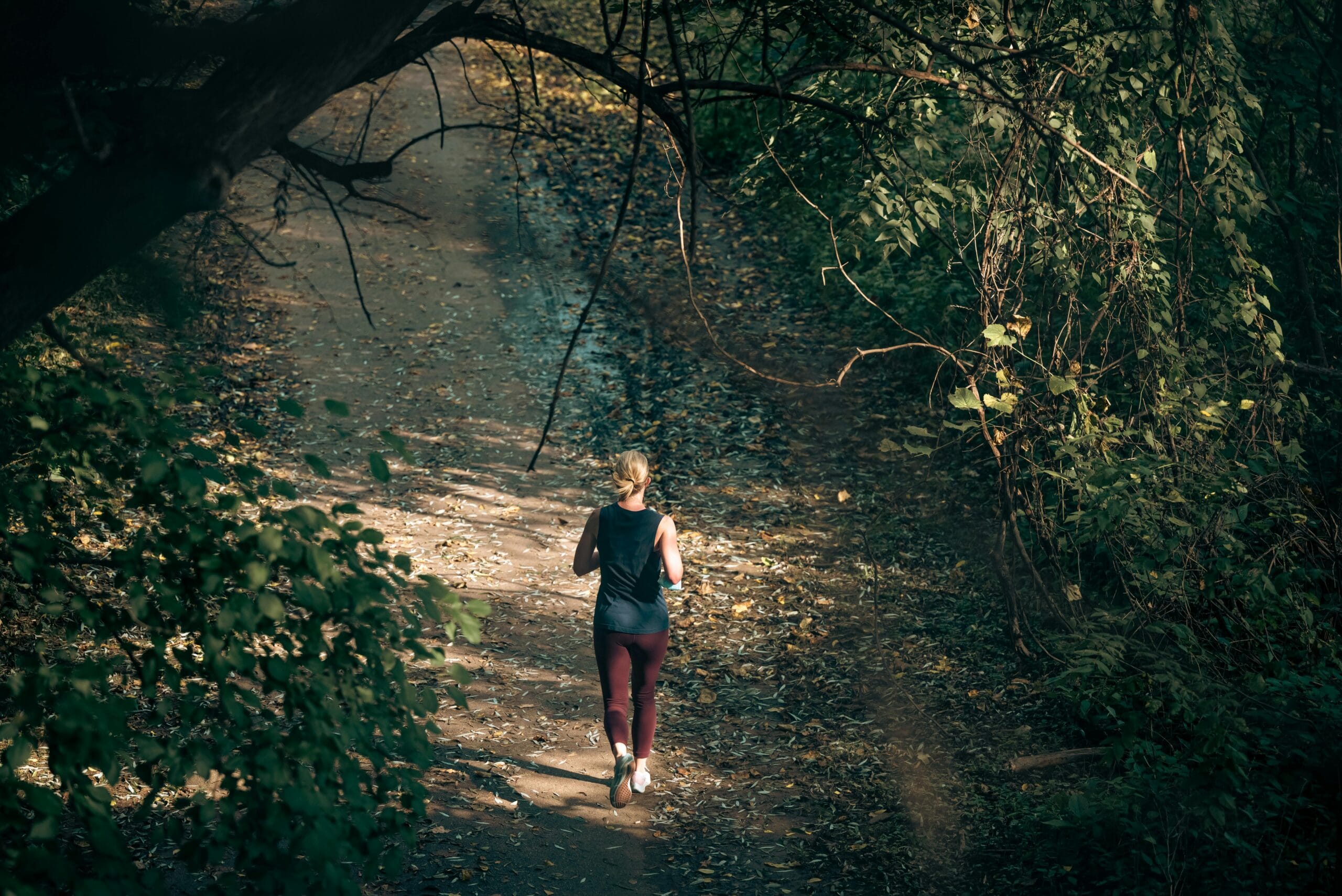 A woman jogs on a forest pathway, embracing a healthy lifestyle and fitness in nature.